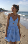 Woman in a light blue dress standing on a beach with ocean waves in the background