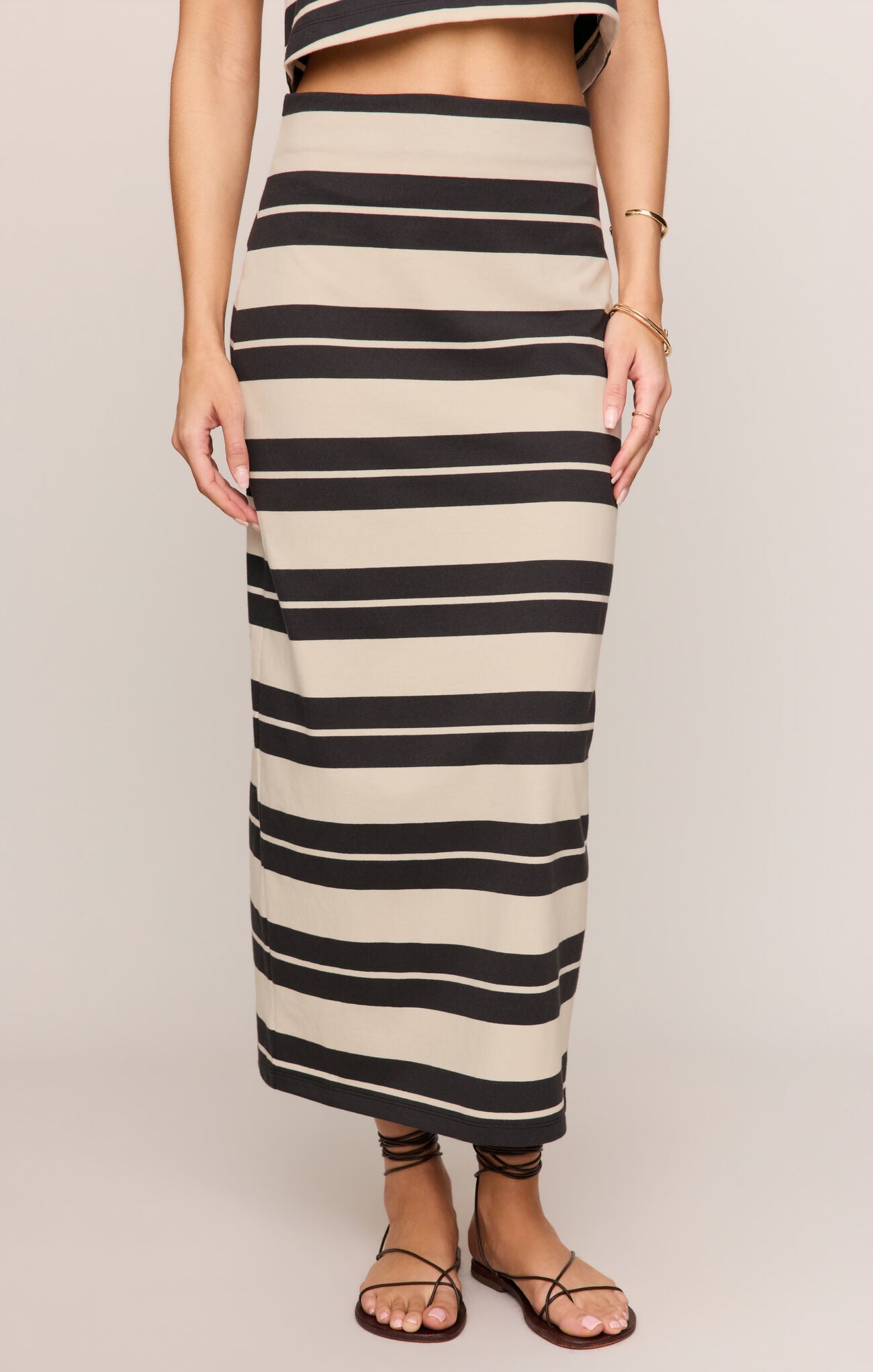 Person wearing a long black and beige striped skirt on a plain background