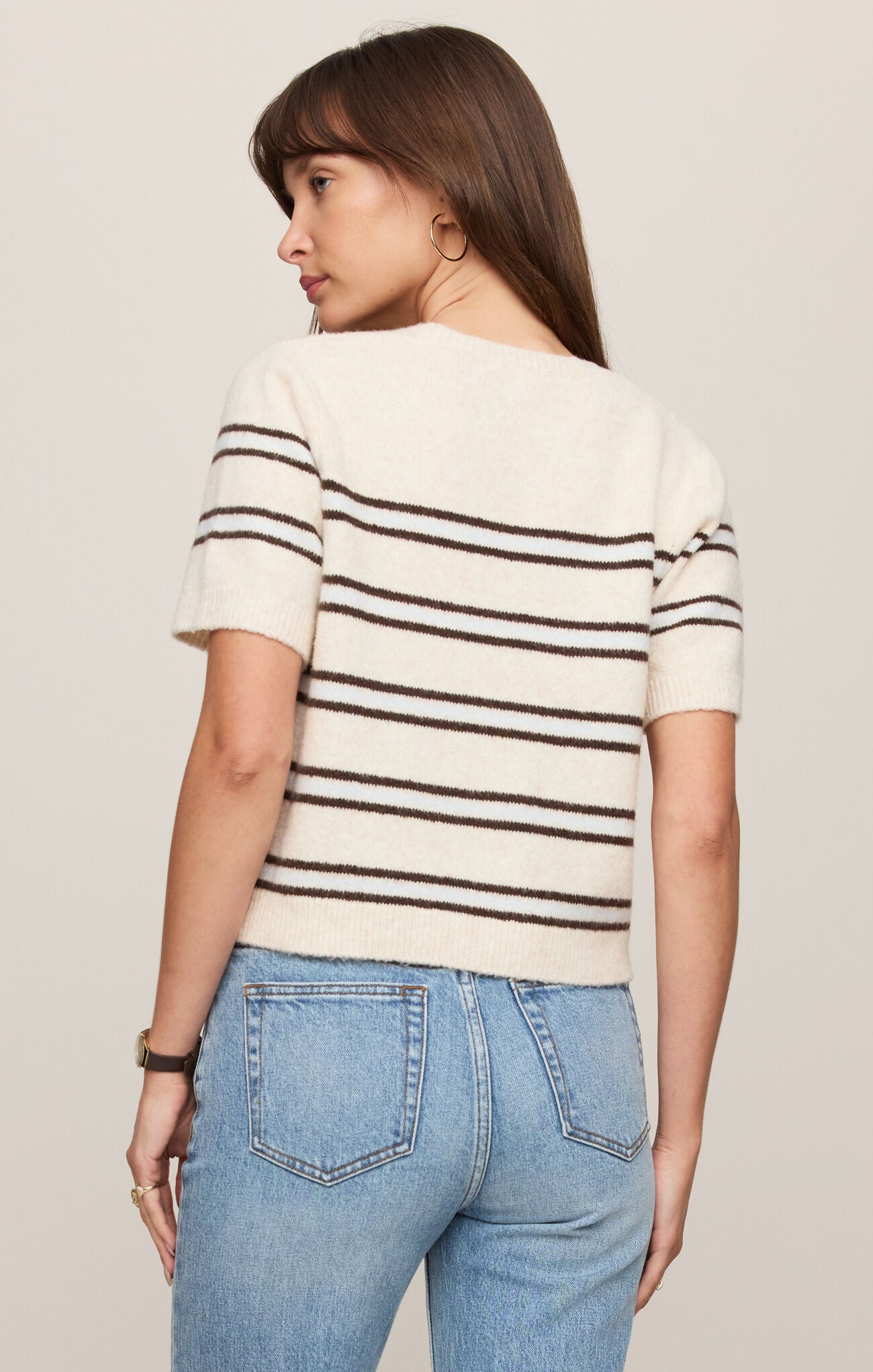 Woman wearing a striped shirt and jeans against a plain background