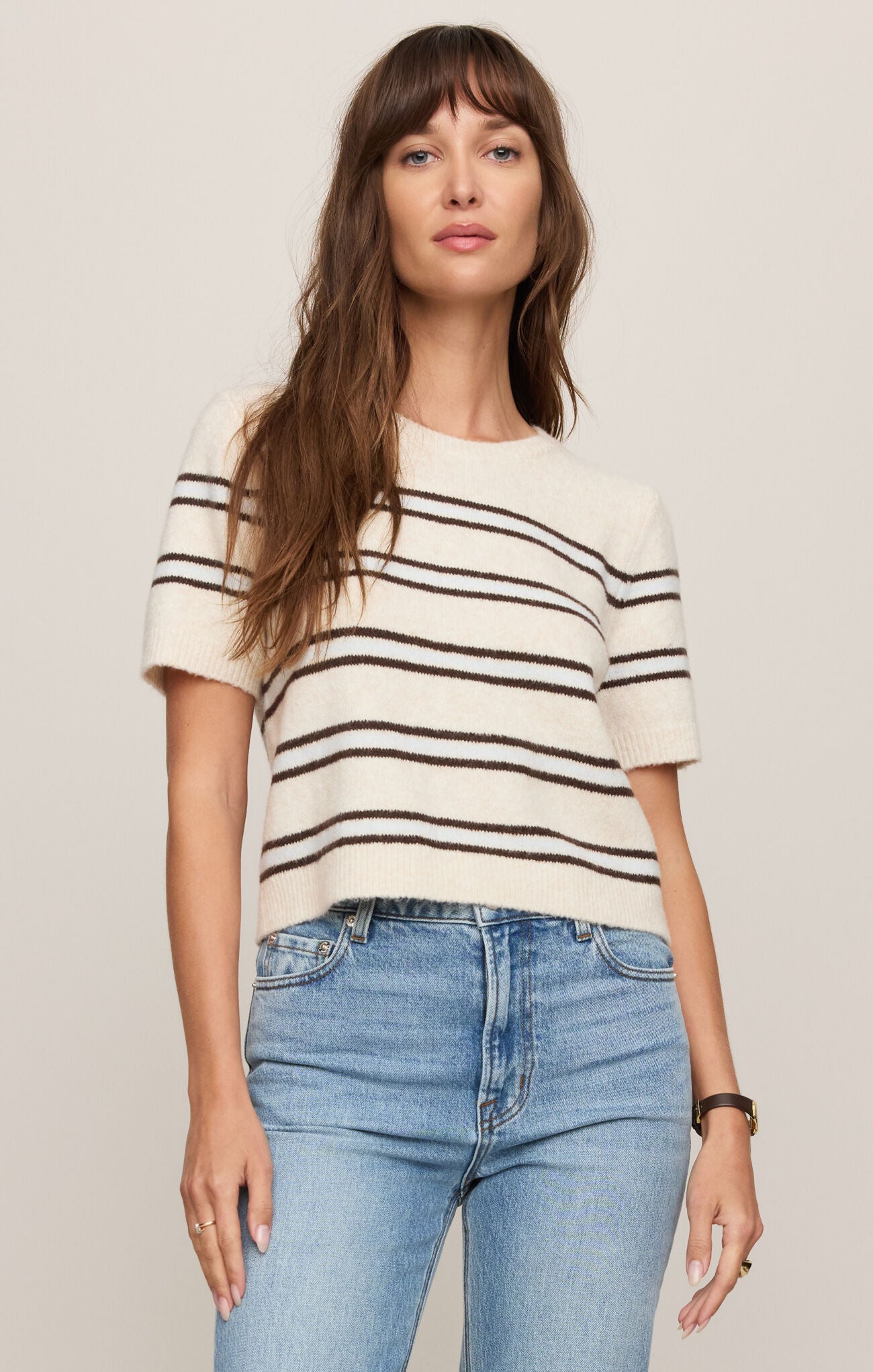 Woman wearing a striped shirt and jeans against a plain background