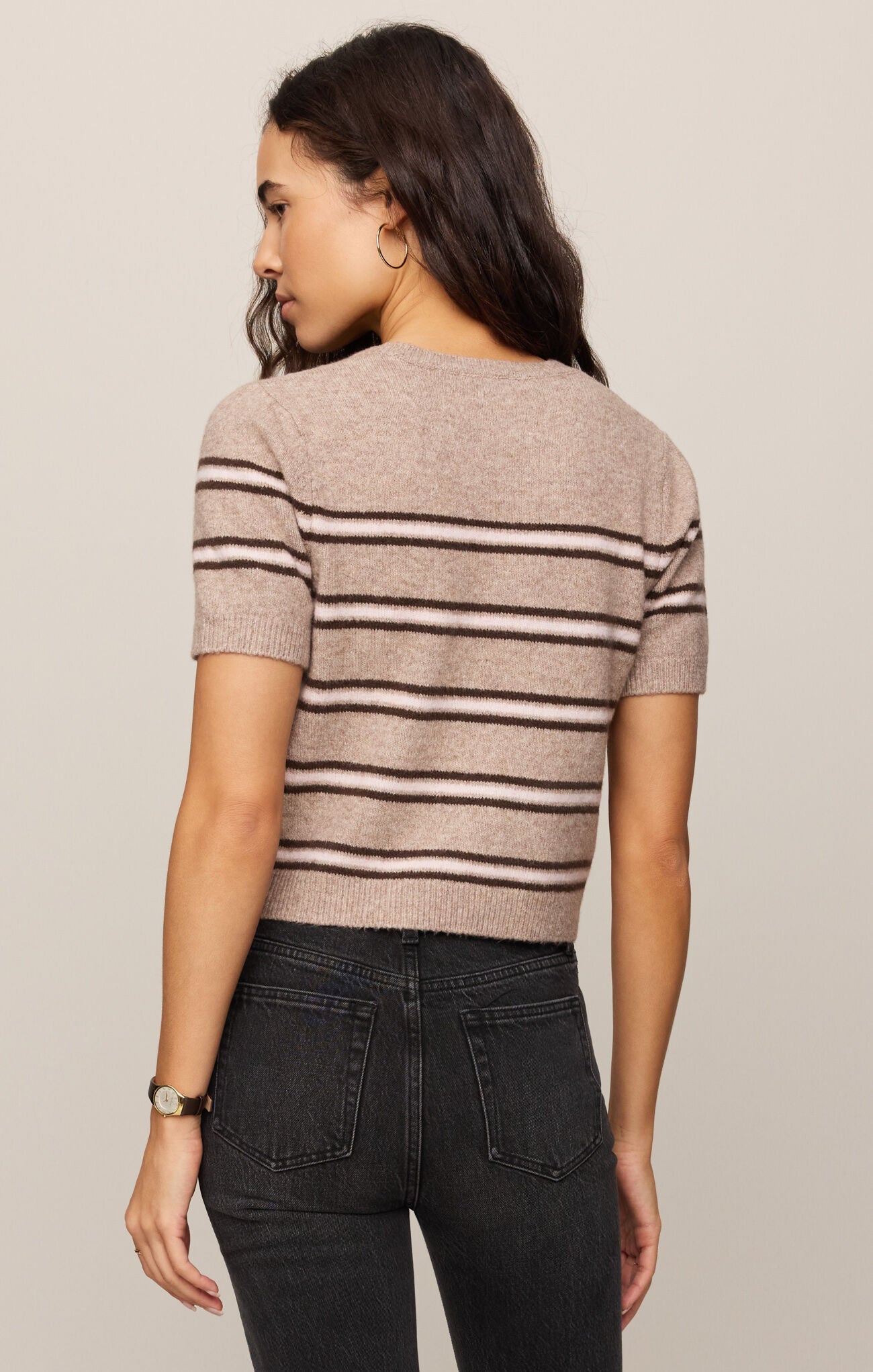 Woman wearing a striped sweater and dark jeans on a plain background