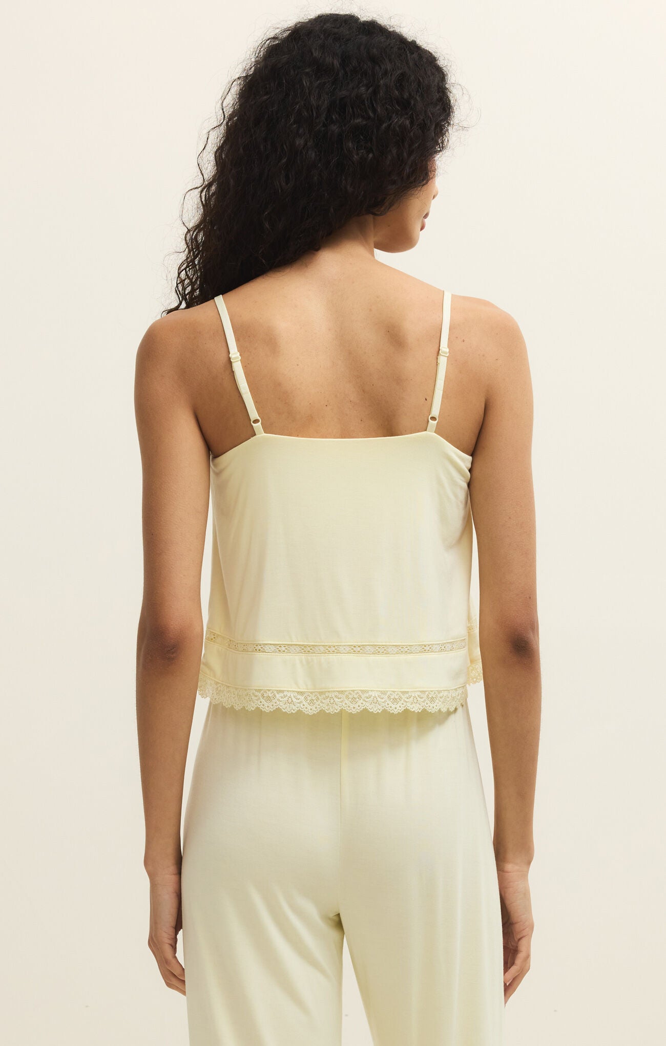 Woman wearing a light green lace-trimmed top and pants on a beige background