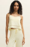 Woman wearing a light yellow sleeveless top and pants on a plain background