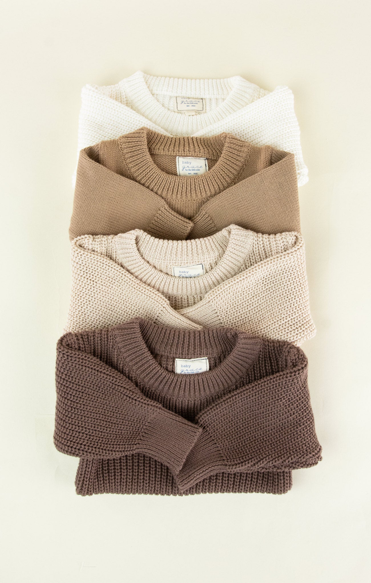 Stack of folded sweaters in brown, beige, and white on a light background
