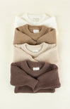 Stack of folded sweaters in brown, beige, and white on a light background