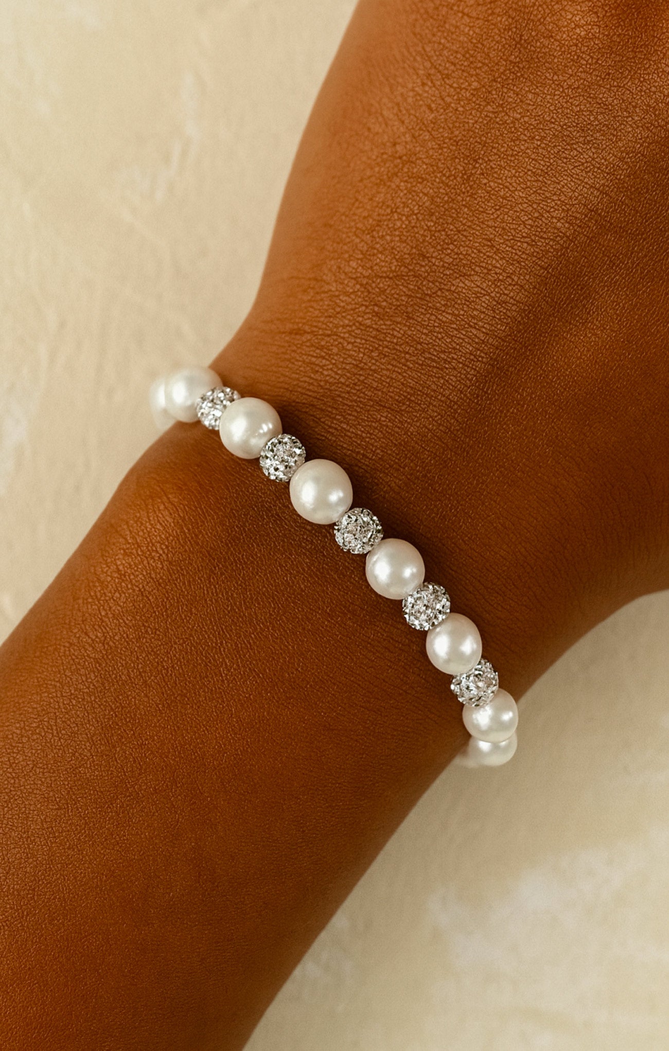 Pearl bracelet with crystals on a wrist against a neutral background