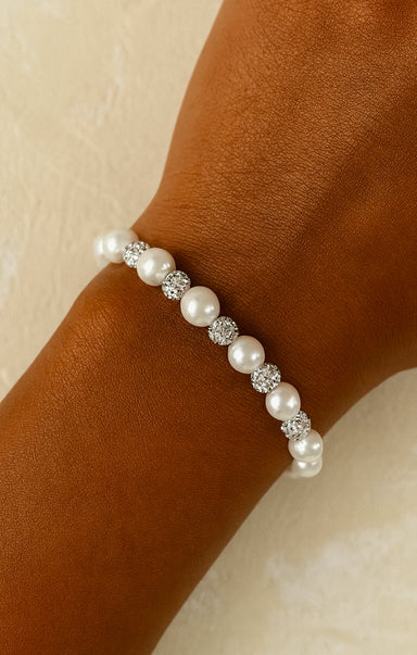 Pearl bracelet with crystals on a wrist against a neutral background