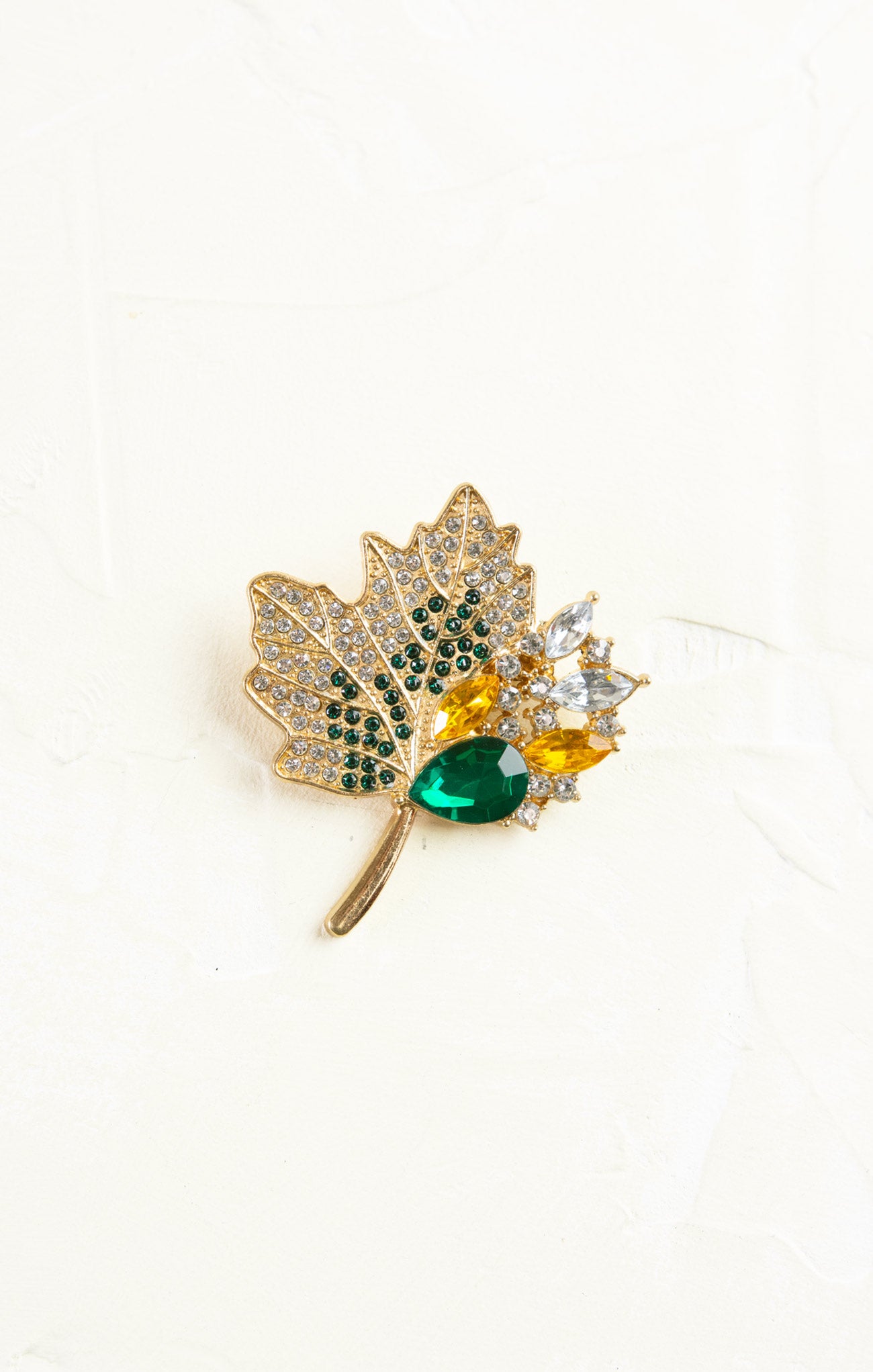 Gold leaf-shaped brooch with gemstones on a white background