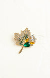 Gold leaf-shaped brooch with gemstones on a white background