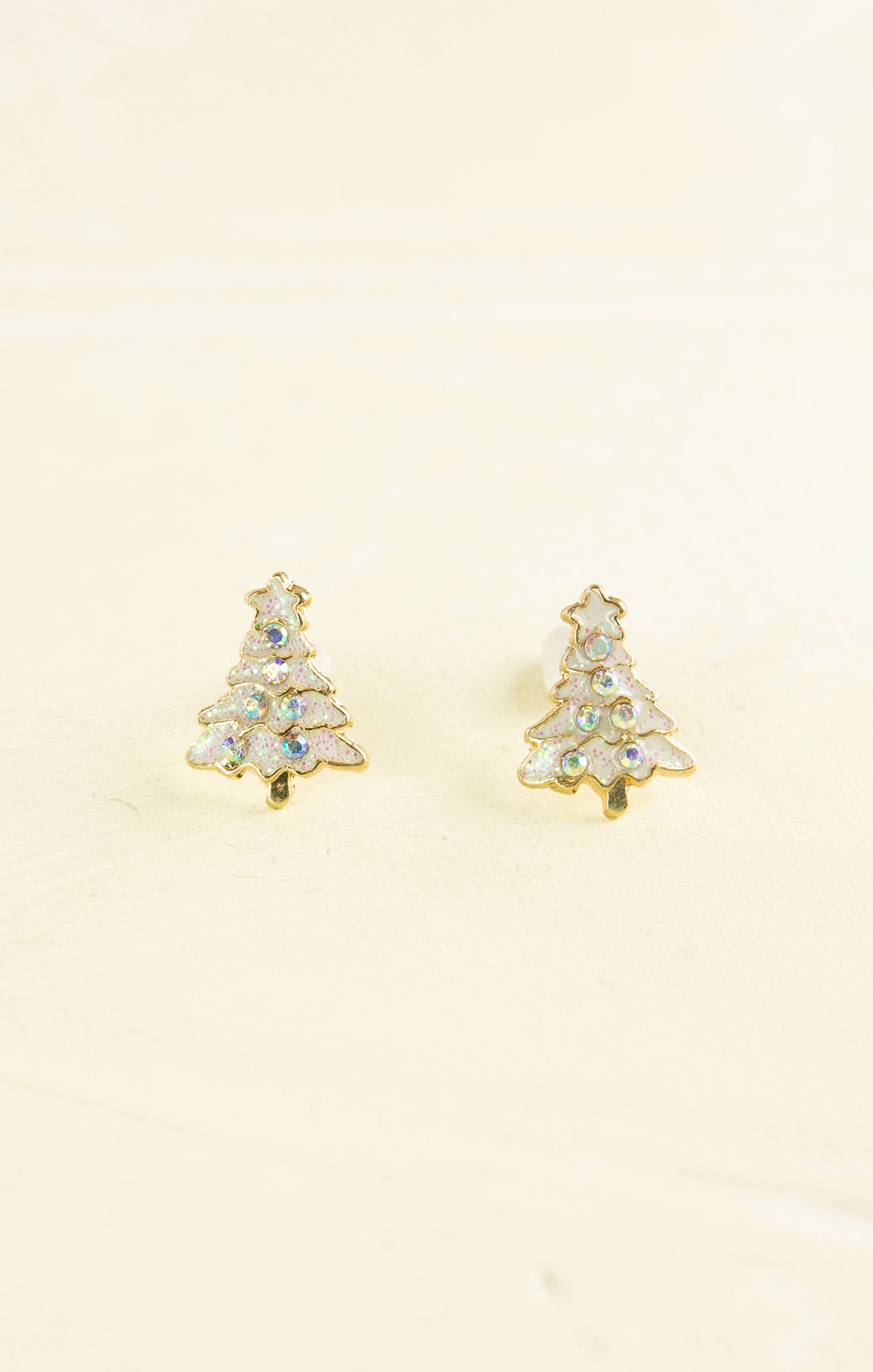 Gold tree-shaped earrings with clear gemstones on a beige background