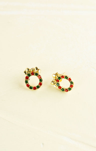 Gold earrings with red and green gemstones on a beige background