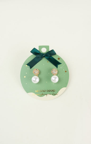 Pair of pearl earrings on a green card with a bow, on a light beige background