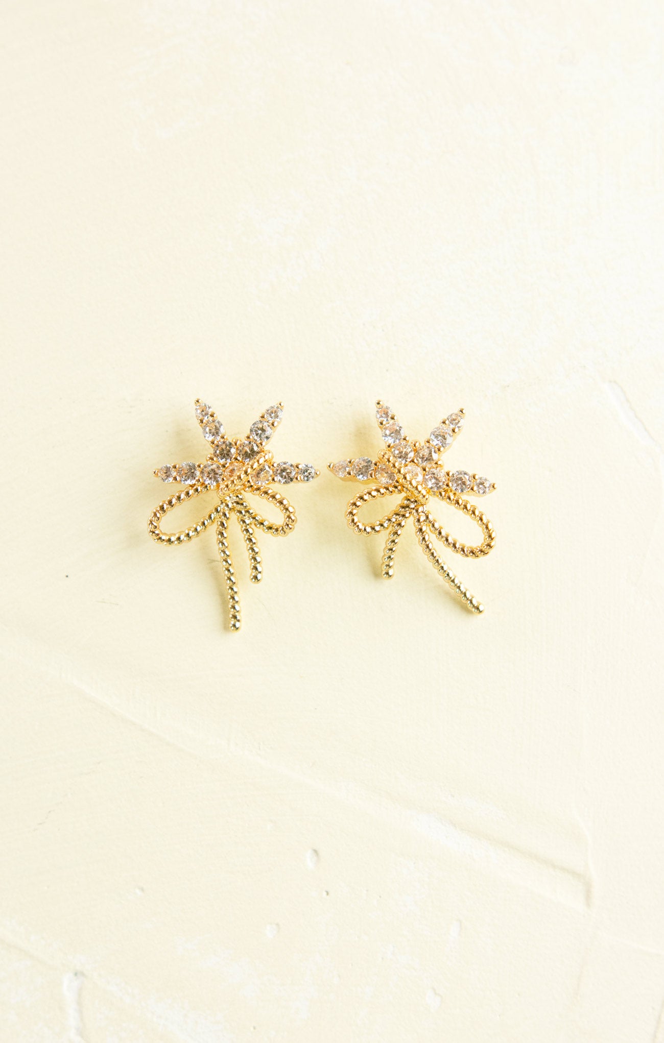 Gold bow-shaped earrings on a beige background