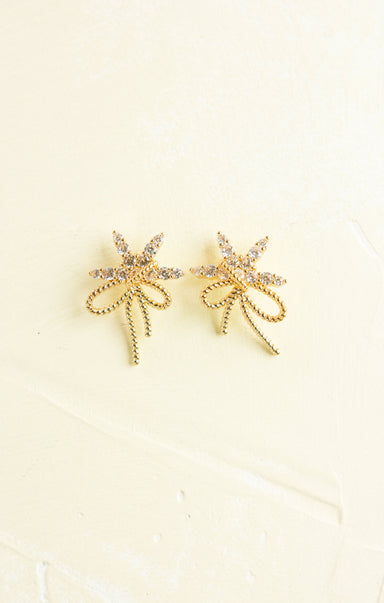 Gold bow-shaped earrings on a beige background