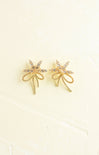 Gold bow-shaped earrings on a beige background