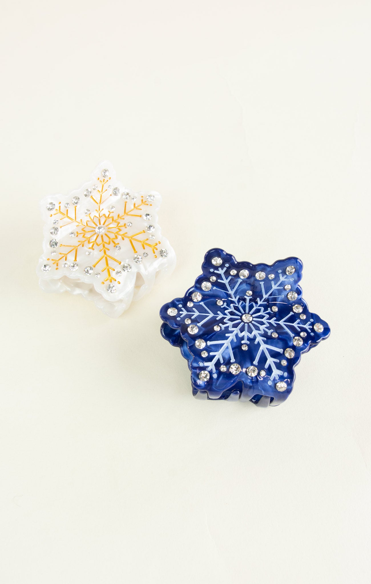 Two snowflake-shaped decorative items, one blue and one white with gold accents, on a light beige background.