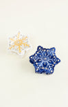 Two snowflake-shaped decorative items, one blue and one white with gold accents, on a light beige background.