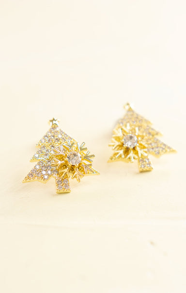 Gold tree-shaped earrings with clear gemstones on a beige background