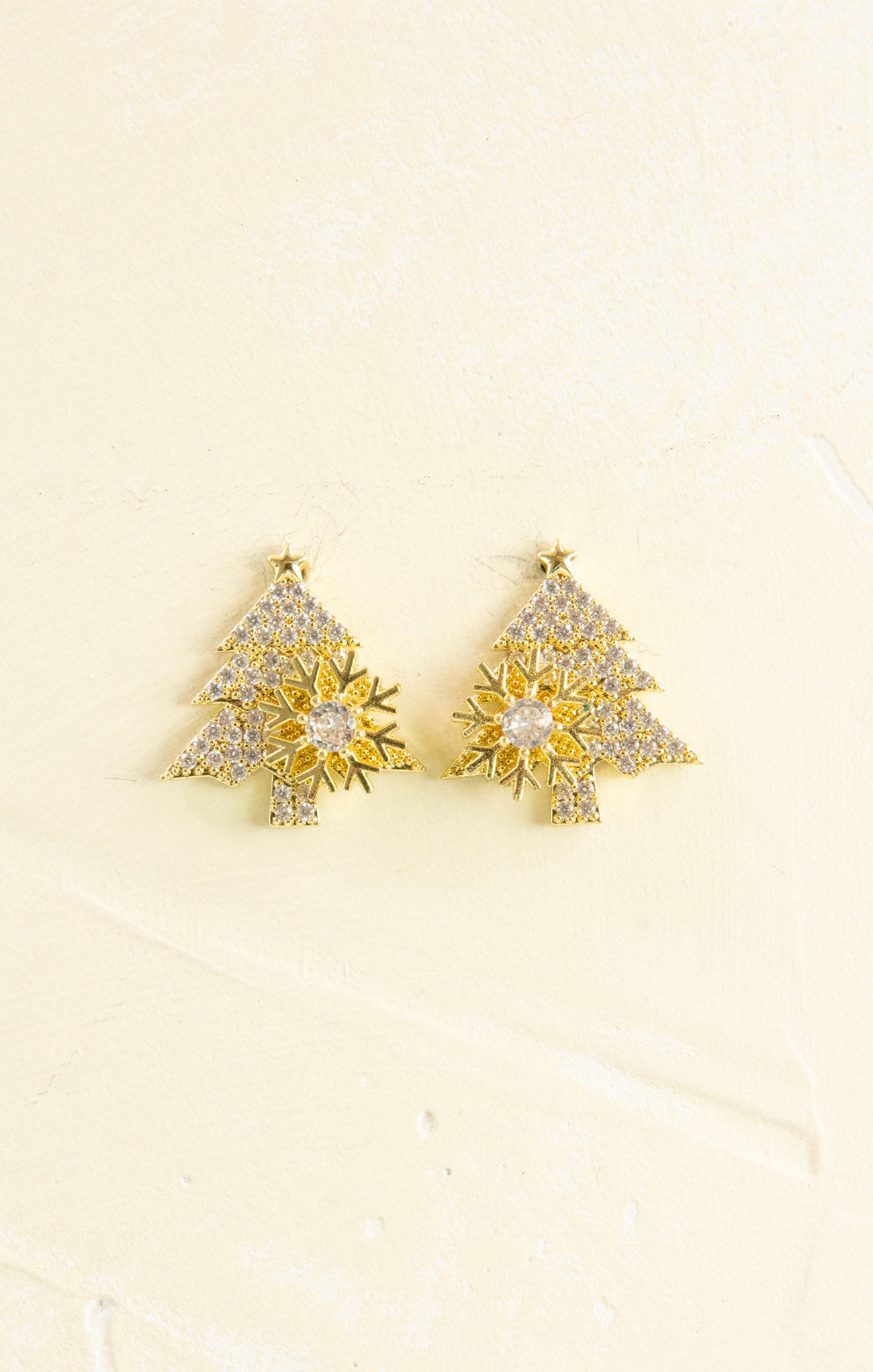 Gold tree-shaped earrings with clear stones on a beige background