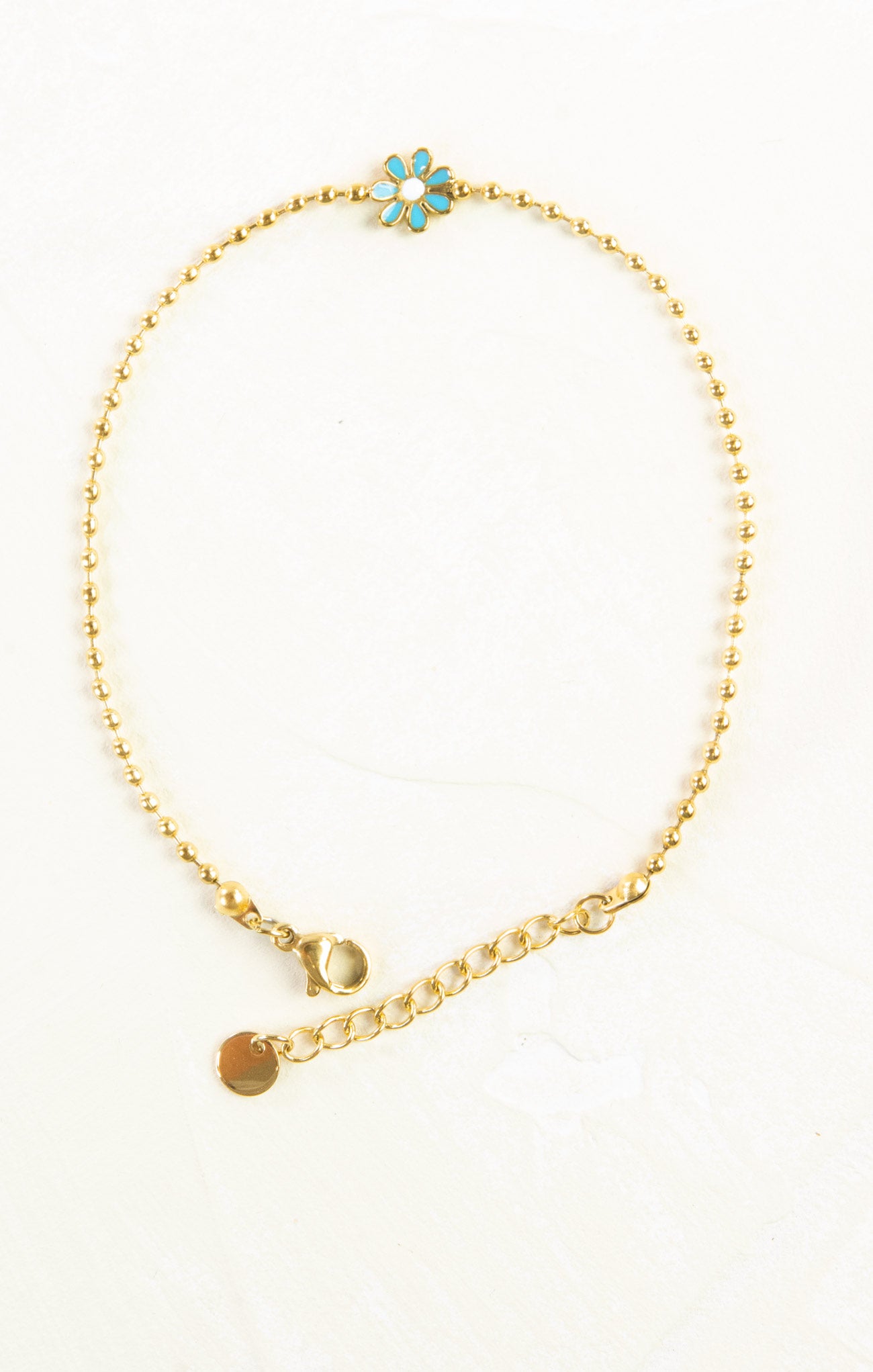 Gold anklet with turquoise flower charm on a white background
