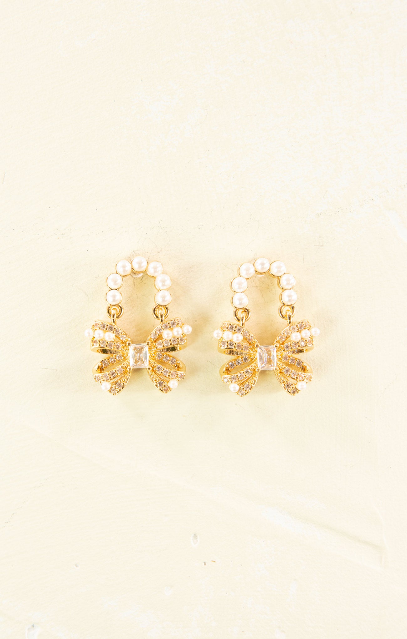 Pair of gold earrings with pearl accents on a beige background