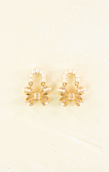 Pair of gold earrings with pearl accents on a beige background