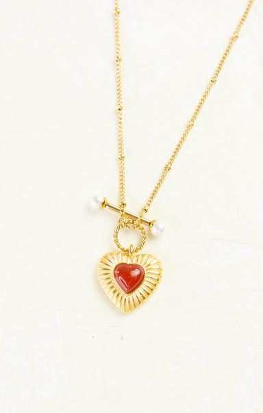 Gold necklace with a heart-shaped red pendant on a white background