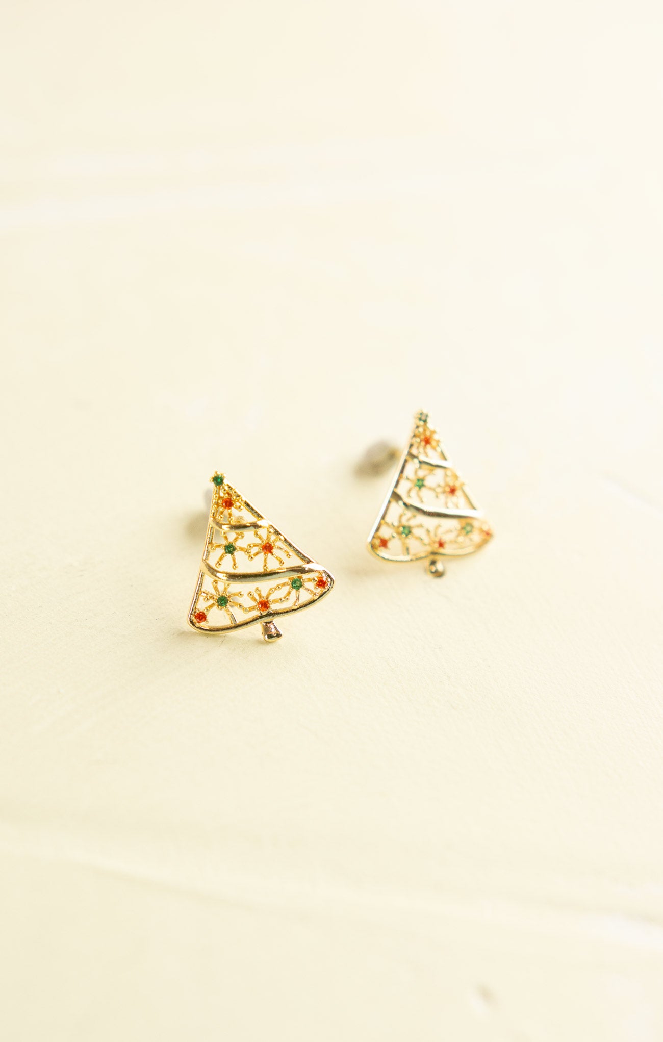 Pair of gold Christmas tree-shaped earrings on a beige background