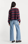 A model shown from the back wearing a cropped, long-sleeve knit sweater with horizontal burgundy and navy stripes, paired with wide-leg light blue jeans and dark loafers, against a plain white studio background.