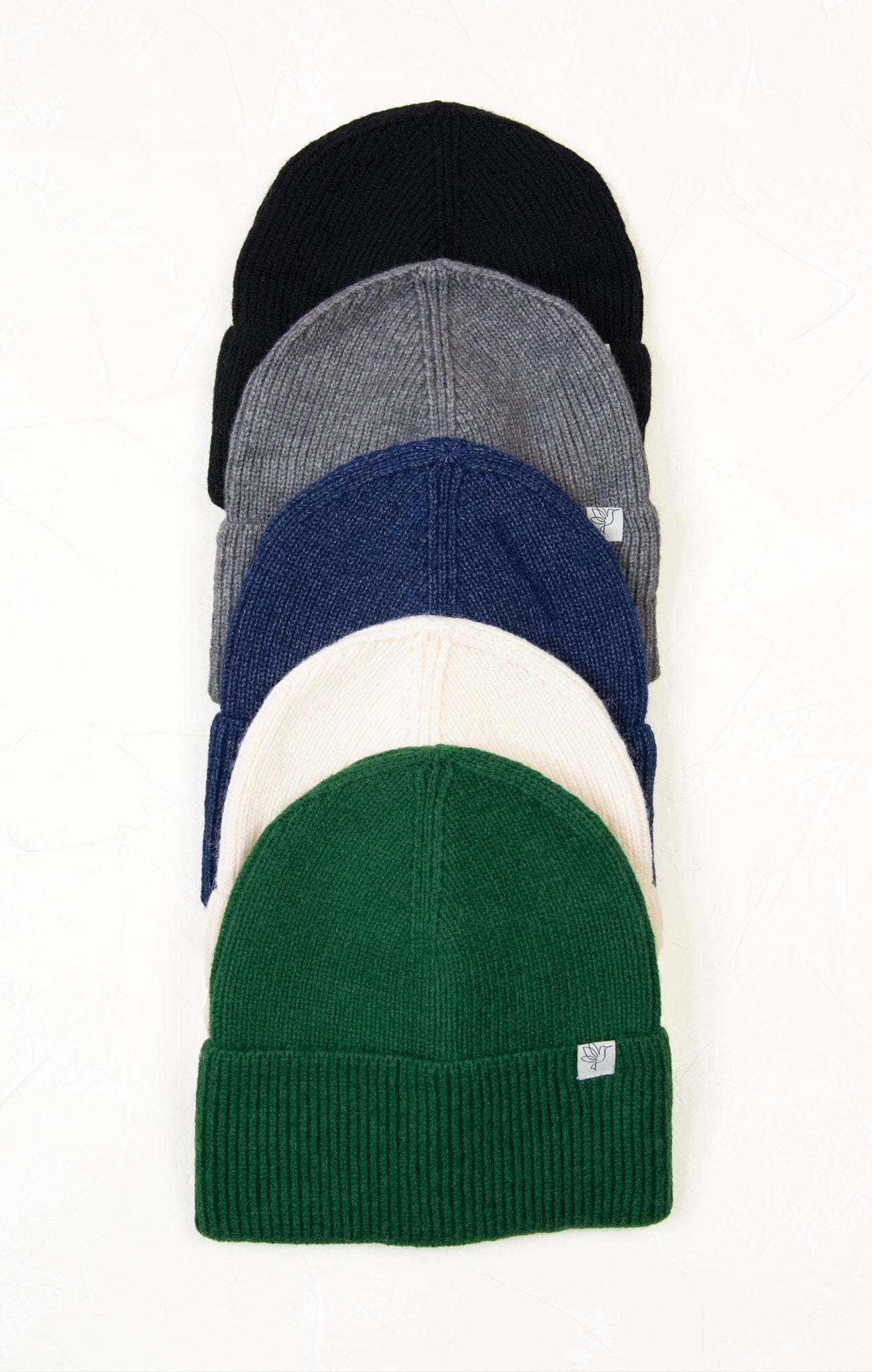 Stack of five knit beanie hats in black, gray, blue, white, and green on a white background.