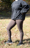 Person wearing a dark gray sweatshirt with text, dark leggings, and sneakers outdoors.