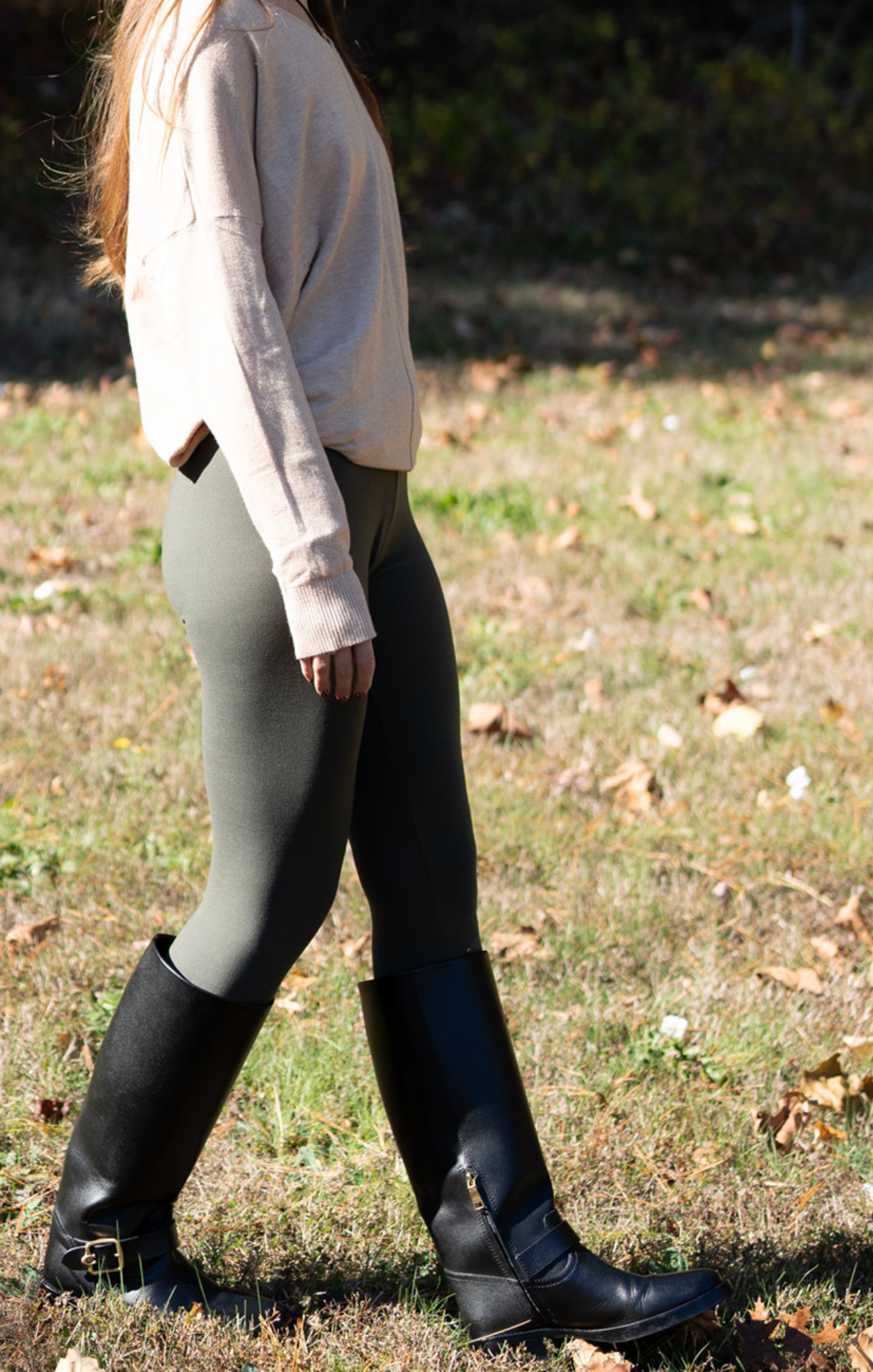 Person wearing black knee-high boots and gray leggings walking on grass.