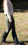 Person wearing black knee-high boots and gray leggings walking on grass.