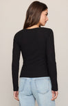 A woman shown from the back wearing a fitted black long-sleeve top and light blue jeans against a plain light beige studio background.