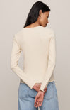 Woman wearing a cream sweater and blue jeans against a plain background
