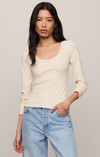 Woman wearing a beige long-sleeve top and light blue jeans against a plain background
