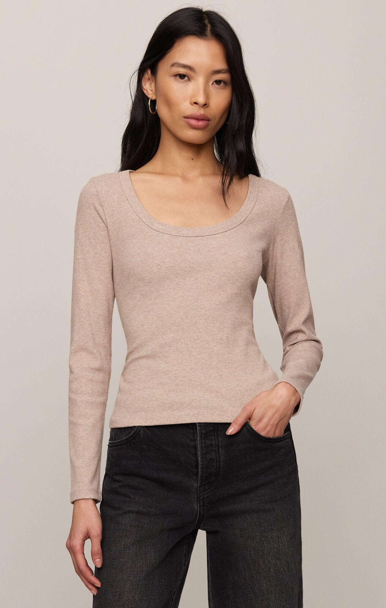 Woman wearing a beige long-sleeve top and black pants against a plain background
