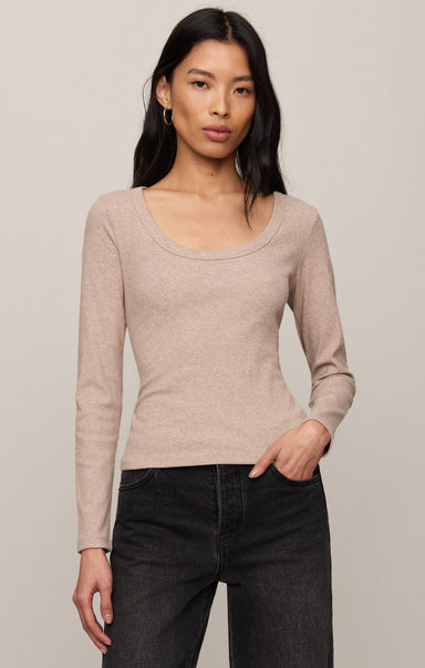 Woman wearing a beige long-sleeve top and black pants against a plain background