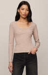 Woman wearing a beige long-sleeve top and black pants against a plain background