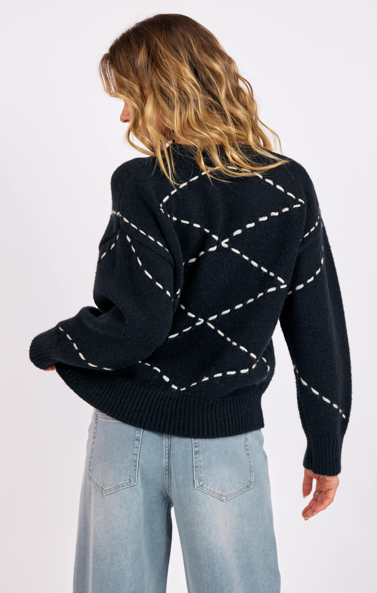 Person wearing a black sweater with white stitching pattern on a plain background
