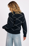 Person wearing a black sweater with white stitching pattern on a plain background