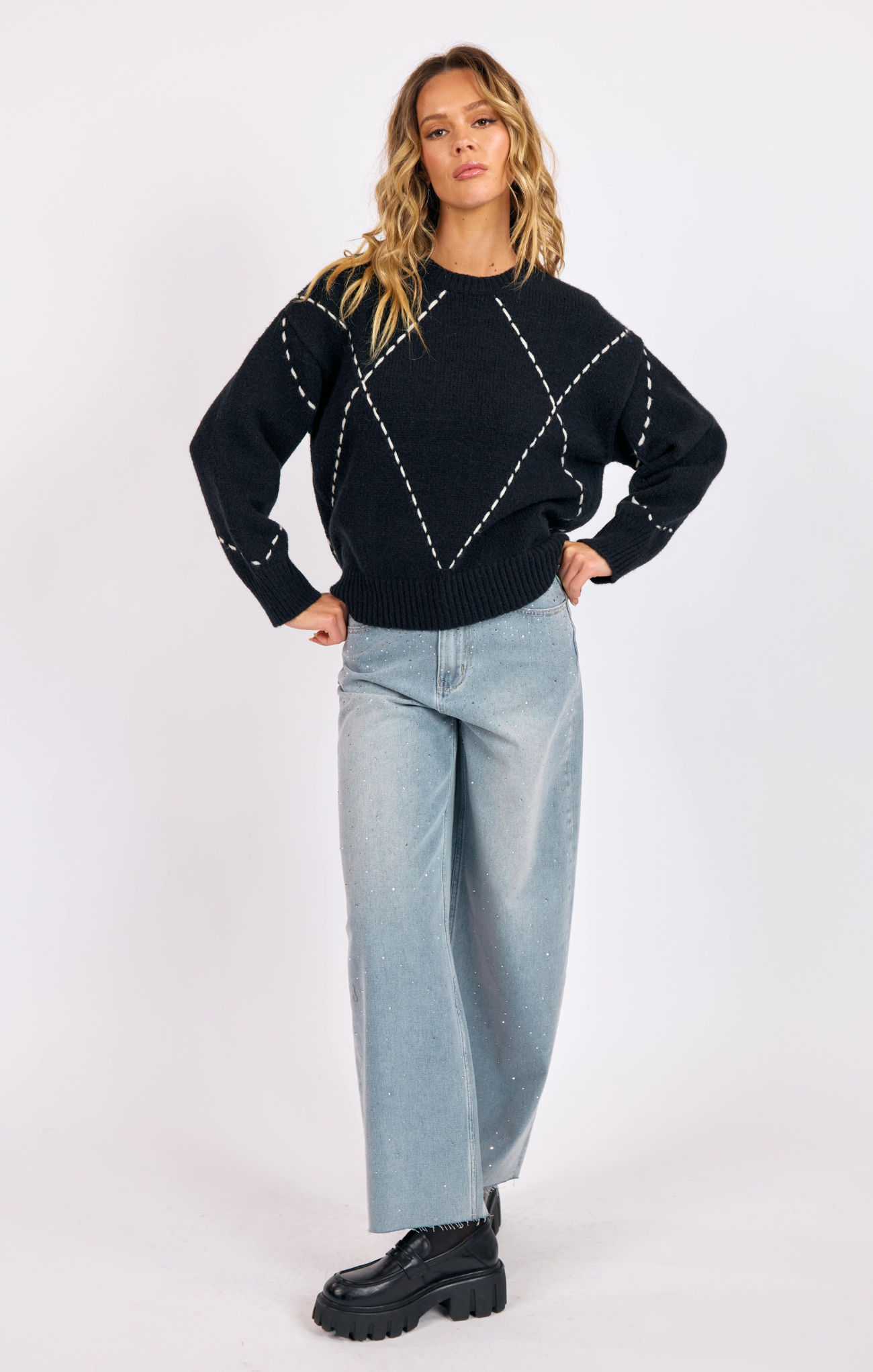 Woman wearing a black sweater with white patterns and light blue jeans on a white background