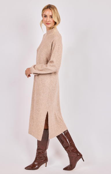 Woman wearing a beige long sweater dress with brown boots on a white background