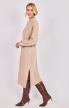 Woman wearing a beige long sweater dress with brown boots on a white background