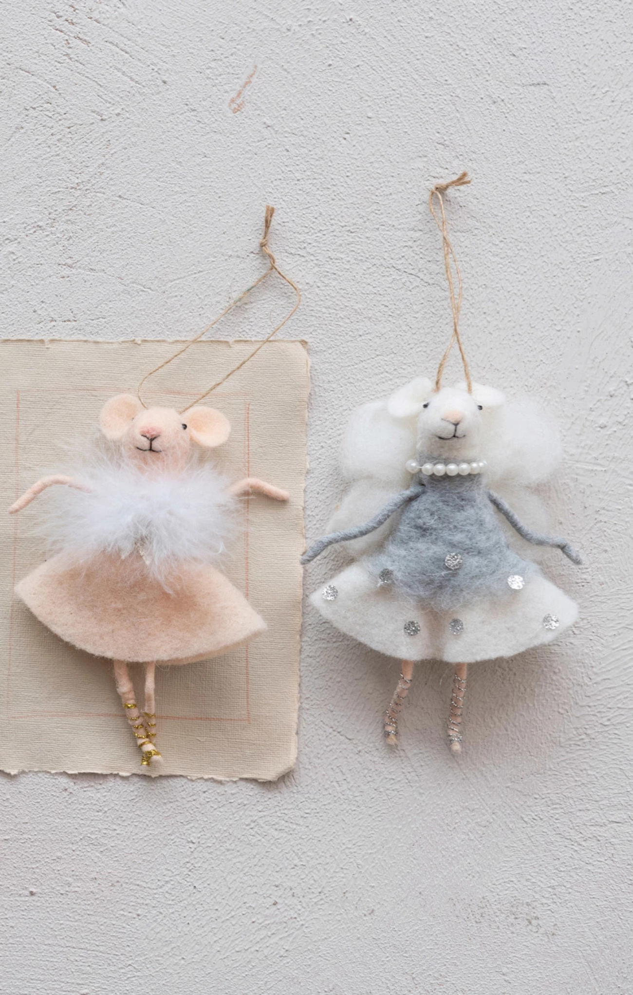 Two decorative mouse figurines in dresses hanging on a textured wall.