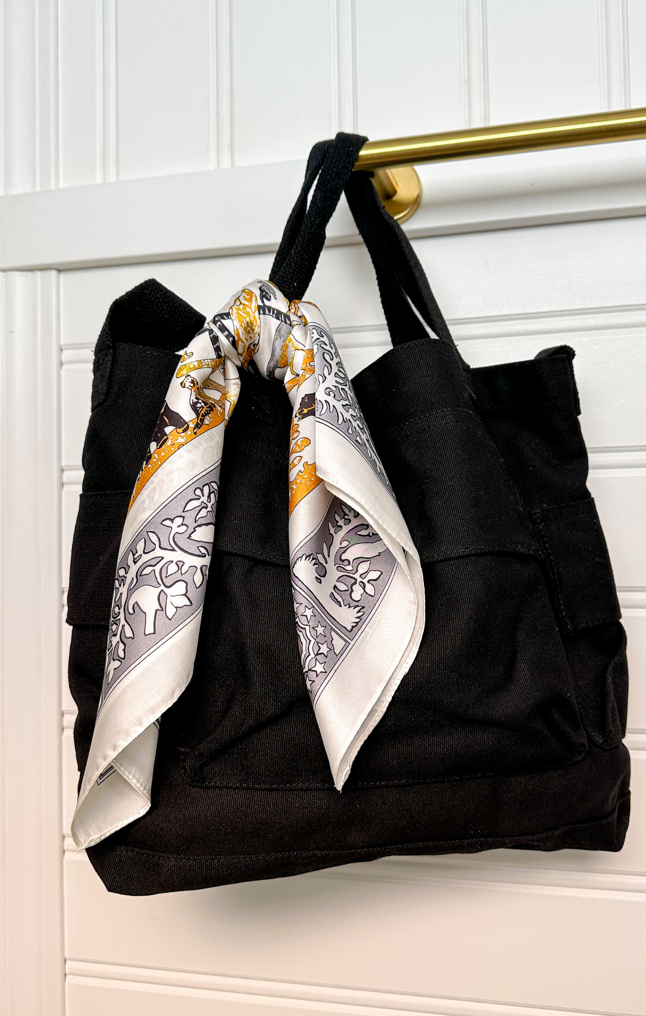 Black tote bag with a decorative scarf draped over it against a white background