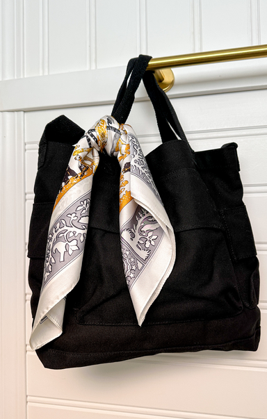 Black tote bag with a decorative scarf draped over it against a white background