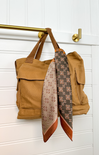 Brown bag with a patterned scarf draped over it against a white background