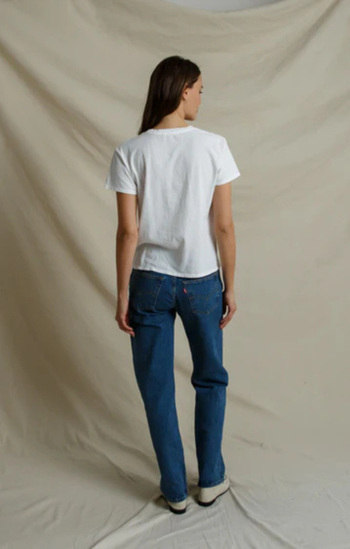 A model shown from the back wearing a white short-sleeve t-shirt and blue jeans, standing against a draped beige fabric backdrop.