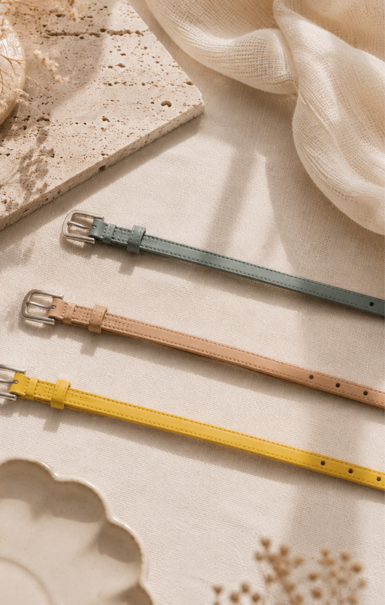 Three leather belts in green, brown, and yellow on a textured surface.